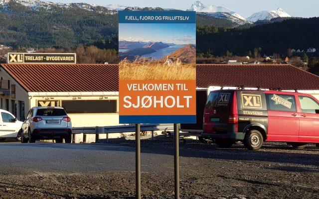 Stort skilt i serien Plano med rette stolper og tekst Velkommen til Sjøholt.